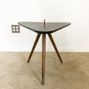 May include: A triangular side table with a black top and three wooden legs with brass tips. The table has a brass ring on the top.
