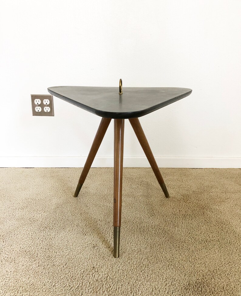 May include: A triangular side table with a black top and three wooden legs with brass tips. The table has a brass ring on the top.