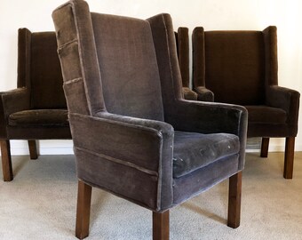 May include: Four brown velvet high-back chairs with wooden legs. The chairs are arranged in a row, with the middle chair in focus.