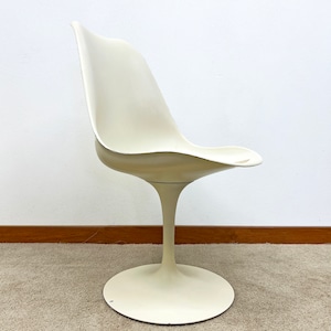 May include: A white tulip chair with a rounded, curved back and a single, wide base. The chair is made of a smooth, white plastic material.