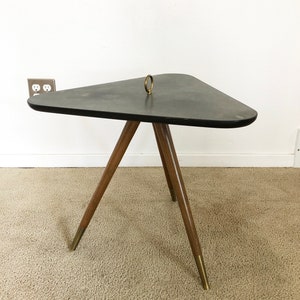 May include: A triangular black side table with a brass ring on top and three wooden legs with brass tips. The table is on a beige carpet.