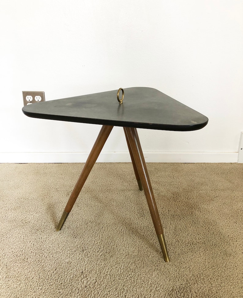 May include: A triangular black side table with a brass ring on top and three wooden legs with brass tips. The table is on a beige carpet.