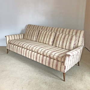 May include: A striped sofa with a beige and pink color scheme. The sofa has four cushions and wooden legs.