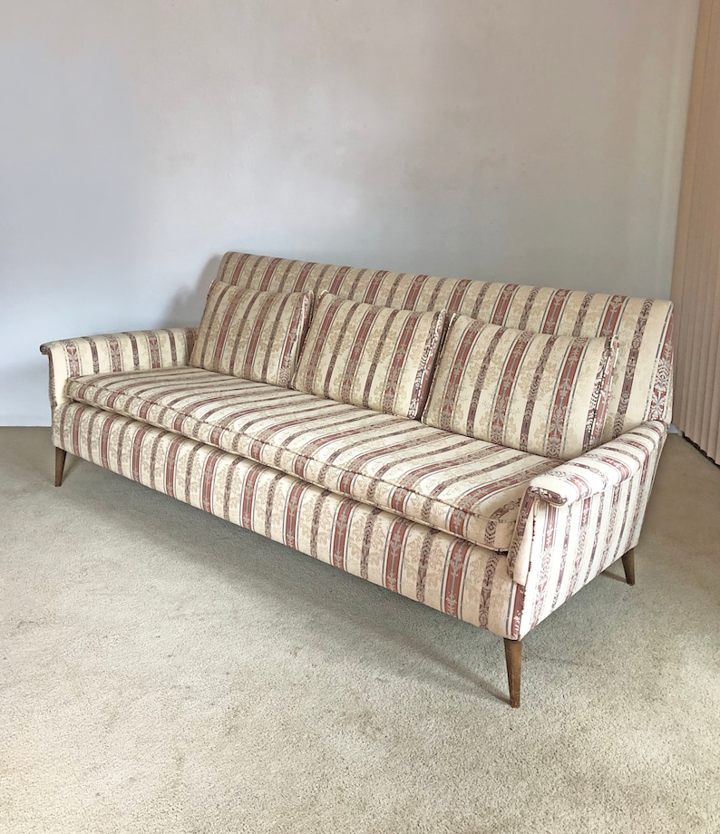 May include: A striped sofa with a beige and pink color scheme. The sofa has four cushions and wooden legs.