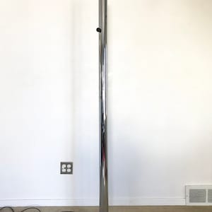 May include: A chrome floor lamp with a long, cylindrical stem and a black, four-pronged base.