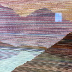 May include: Abstract artwork featuring layered horizontal lines in shades of brown, purple, and blue. The composition suggests a landscape with mountain-like shapes and a light blue area, creating a textured, artistic effect.