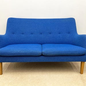 May include: A blue two-seater sofa with a curved back and armrests. The sofa has a tufted backrest and wooden legs. The fabric is a solid blue color. The sofa is approximately 60 inches wide.