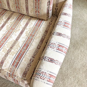 May include: A close-up of a cream-colored sofa with red, blue, and brown striped upholstery. The fabric has a subtle floral pattern.