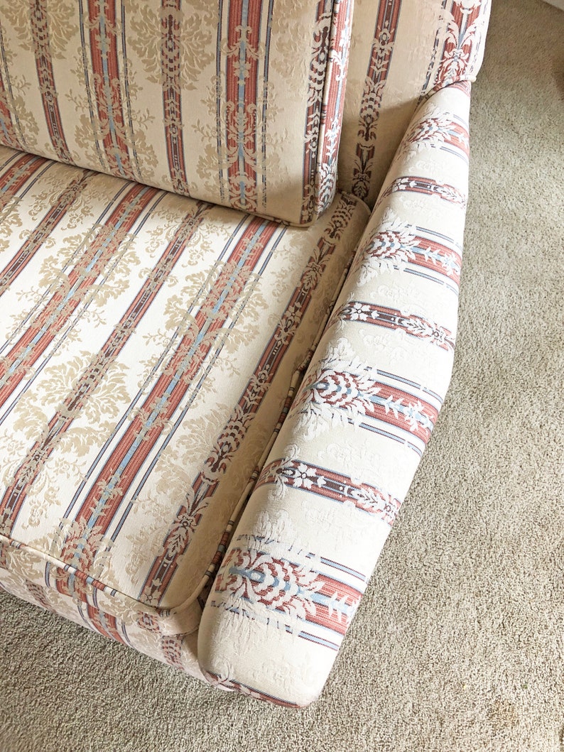 May include: A close-up of a cream-colored sofa with red, blue, and brown striped upholstery. The fabric has a subtle floral pattern.