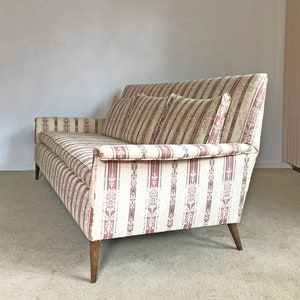 May include: A vintage striped sofa with a beige and brown color scheme. The sofa has a tufted back and wooden legs.