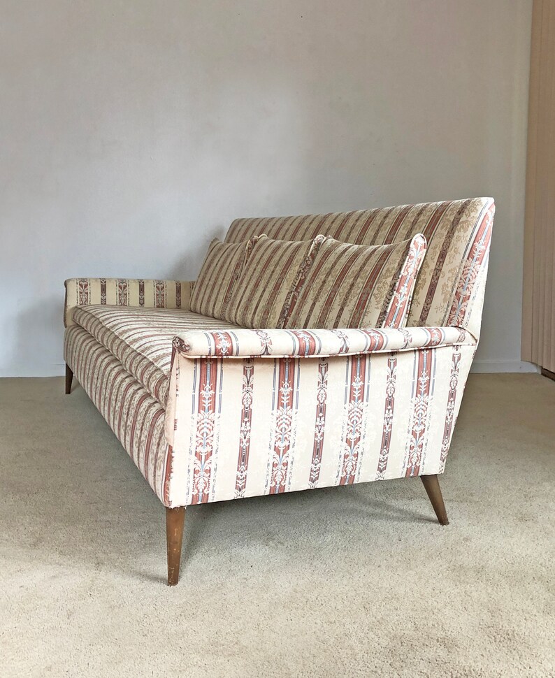 May include: A vintage striped sofa with a beige and brown color scheme. The sofa has a tufted back and wooden legs.