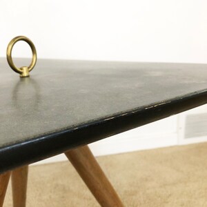 May include: A mid-century modern coffee table with a black laminate top and a brass ring detail. The table has four wooden legs.