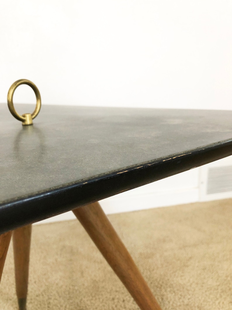 May include: A mid-century modern coffee table with a black laminate top and a brass ring detail. The table has four wooden legs.
