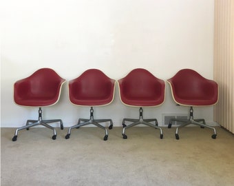 May include: Four red office chairs with silver legs and a white base. The chairs are arranged in a row.