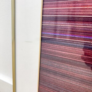 May include: Abstract art print with a gold frame and a white border. The artwork features horizontal lines in shades of red, purple, and brown. The frame has a gold finish, and the white border adds a clean contrast to the colorful artwork.