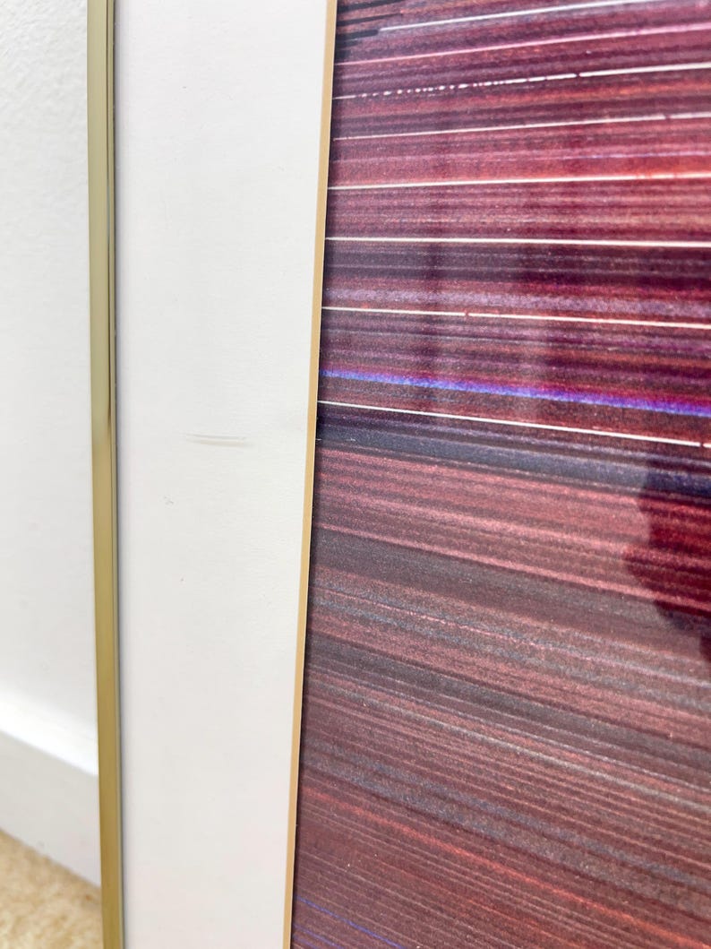 May include: Abstract art print with a gold frame and a white border. The artwork features horizontal lines in shades of red, purple, and brown. The frame has a gold finish, and the white border adds a clean contrast to the colorful artwork.