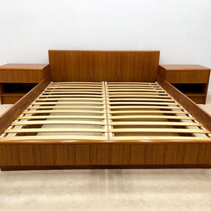 May include: A mid-century modern style bed frame and two matching nightstands. The bed frame is made of wood with a headboard and a slatted base. The nightstands have a single drawer and open shelf. The bed frame is approximately 80 inches long.
