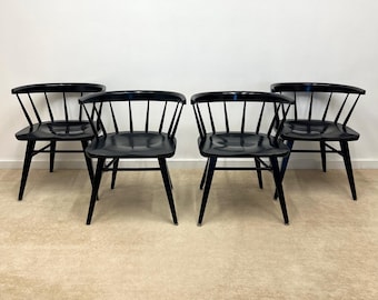 May include: Four black wooden chairs with a spindle back design. The chairs are arranged in a row on a beige carpet.