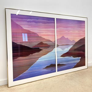 May include: Large framed artwork featuring a landscape scene with mountains, a river, and a sunset. The artwork is divided into two panels and framed in a gold-colored metal frame. The color palette includes shades of purple, blue, and brown.