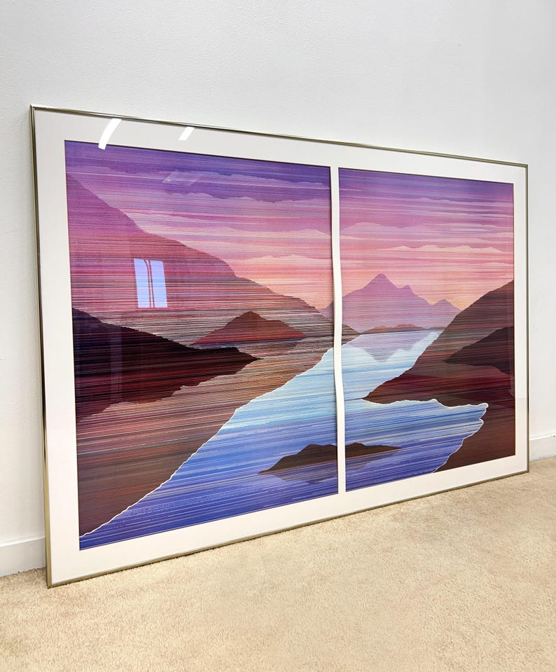 May include: Large framed artwork featuring a landscape scene with mountains, a river, and a sunset. The artwork is divided into two panels and framed in a gold-colored metal frame. The color palette includes shades of purple, blue, and brown.