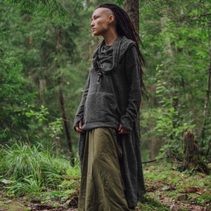 May include: A person with dreadlocks wearing a gray hooded sweater and a long green skirt standing in a forest.