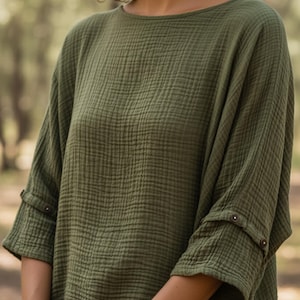 May include: Olive green top with a textured, crinkled fabric. It has a round neckline and three-quarter sleeves with buttoned cuffs. The garment has a relaxed fit, suitable for casual wear. The fabric appears to be a lightweight material.