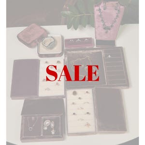 May include: Jewelry display featuring rings, necklaces, and earrings in velvet boxes and on stands. The word "SALE" is prominently displayed in red across the image. Various ring designs include gemstones and intricate settings.