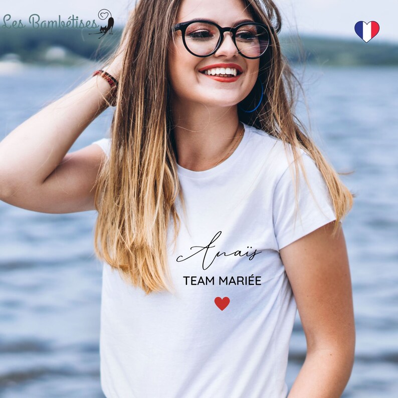 May include: White t-shirt with the text "Ana&iuml;s Team Mari&eacute;e" and a red heart. The shirt is worn by a person with long blonde hair and glasses.