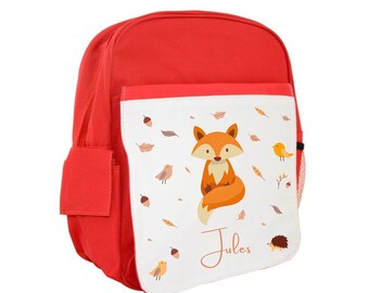 Könnte beinhalten: Roter Kinderrucksack mit einer weißen Fronttasche, die einen Comic-Fuchs, Vögel und Blätter zeigt. Die Tasche trägt auch den Namen "Jules".