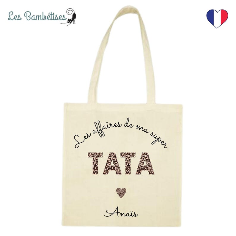 Op de afbeelding: Een beige tote bag met zwarte tekst die "Les affaires de ma super TATA" luidt met een luipaardprint. De tekst "Anais" is onder het ontwerp gedrukt.
