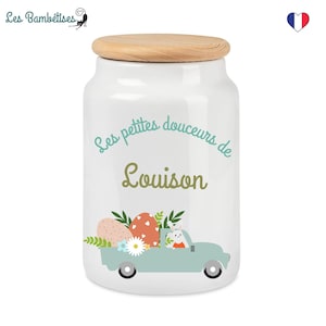 Peut inclure: Pot en céramique blanche avec un couvercle en bois. Le pot est décoré d'un motif bleu et vert avec un lapin conduisant un camion transportant des œufs de Pâques. Le texte sur le pot est "Les petites douceurs de Louison".