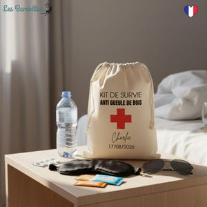 Peut inclure: Un sac en coton beige avec cordon de serrage portant l'inscription "KIT DE SURVIE ANTI GUEULE DE BOIS" et une croix rouge. Le sac porte également le nom "Charlie" et la date "17/08/2026". Une bouteille d'eau, des pilules, un masque de sommeil et des lunettes de soleil sont également présents.
