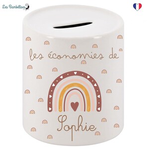 May include: White ceramic money box with a rainbow design and the text "les &eacute;conomies de Sophie". The rainbow is in shades of pink, orange, and yellow with brown hearts.