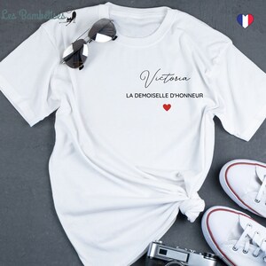 May include: White t-shirt with the name "Victoria" and the text "La Demoiselle d'Honneur" in black lettering with a red heart.