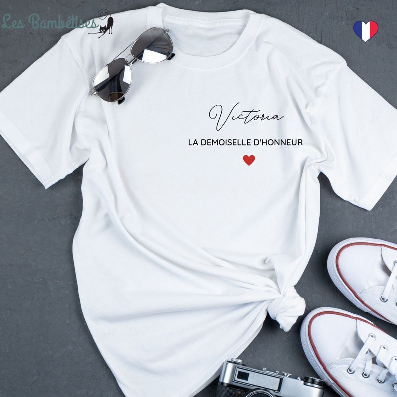 May include: White t-shirt with the name "Victoria" and the text "La Demoiselle d'Honneur" in black lettering with a red heart.