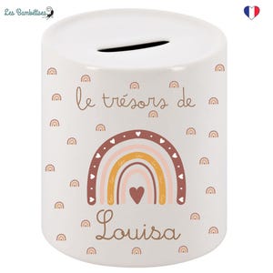 May include: White ceramic money box with a rainbow design and the text "le tr&eacute;sors de Louisa". The rainbow is in shades of pink, orange, and yellow with brown outlines and white hearts. The background is white with a scattered pattern of small brown rainbows.