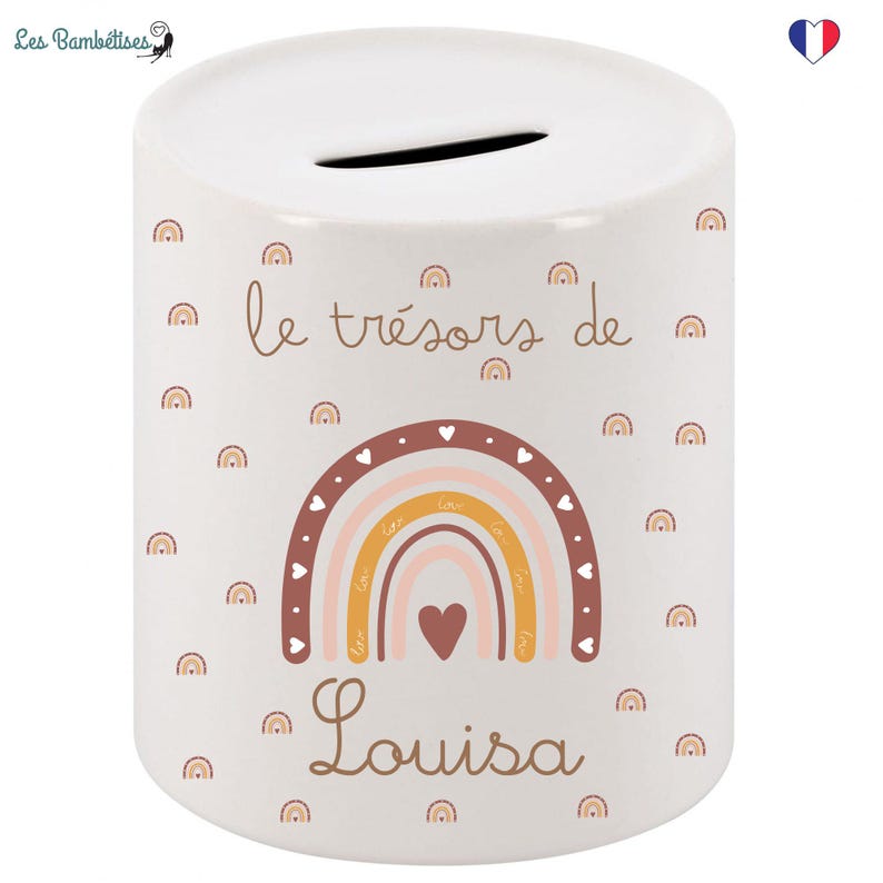 May include: White ceramic money box with a rainbow design and the text "le tr&eacute;sors de Louisa". The rainbow is in shades of pink, orange, and yellow with brown outlines and white hearts. The background is white with a scattered pattern of small brown rainbows.