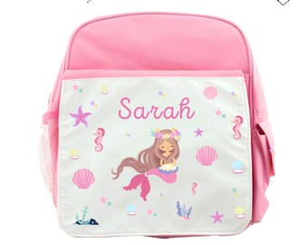 Könnte beinhalten: Rosa Rucksack mit einer weißen Fronttasche, die eine Meerjungfrauen-Illustration, Muscheln und Sterne zeigt. Der Name "Sarah" ist auf der Tasche aufgedruckt.