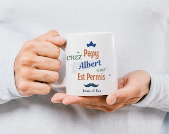 May include: White ceramic mug with a blue and orange design. The mug says "Chez Papy Albert Tout Est Permis" with a crown, mustache, and the words "Louis et Eva".