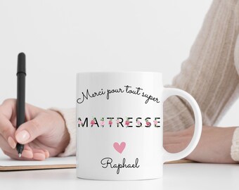 May include: White ceramic mug with a black floral design that says "Merci pour tout super MAITRESSE" with a pink heart and the name "Raphael" below.