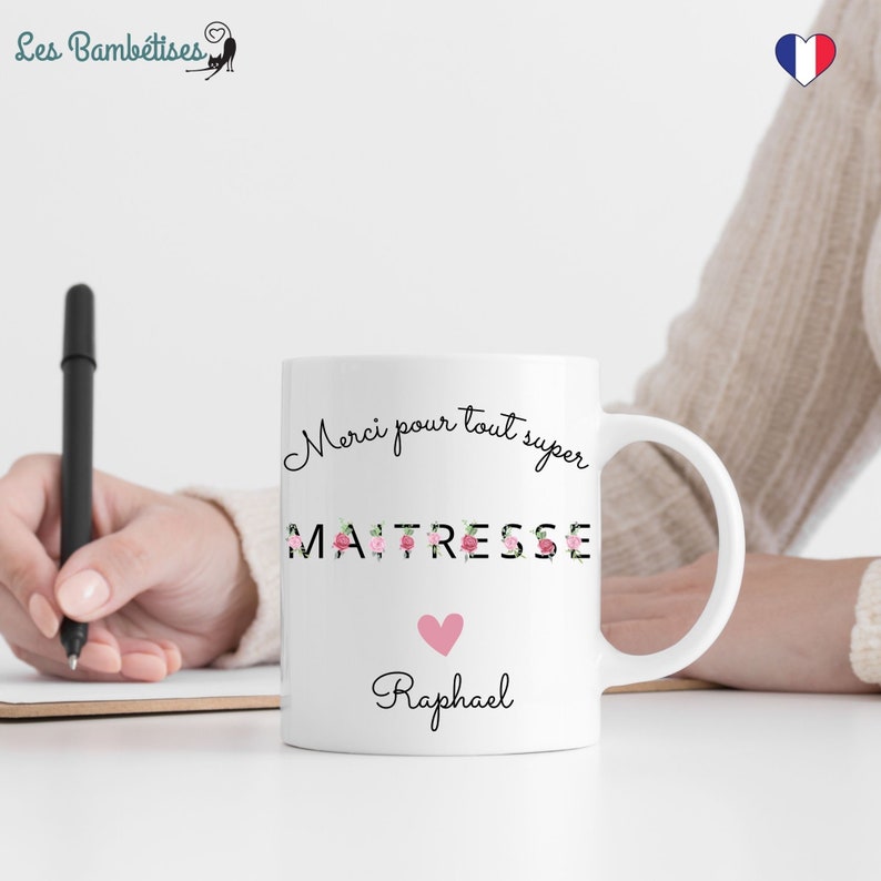 Puede incluir: Taza de cer&aacute;mica blanca con un dise&ntilde;o floral negro que dice "Merci pour tout super MAITRESSE" con un coraz&oacute;n rosa y el nombre "Raphael" debajo.