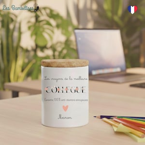 May include: A white ceramic pencil holder with a wooden lid. The text on the holder reads "Les crayons de la meilleure COLLEAGUE" with additional text and a heart symbol. A name is written below the heart. Pencils and a laptop are in the background.