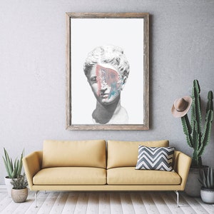 May include: A framed print of a white plaster bust of a woman with a colorful abstract paint splatter covering part of her face. The print is hanging on a gray wall above a yellow sofa.