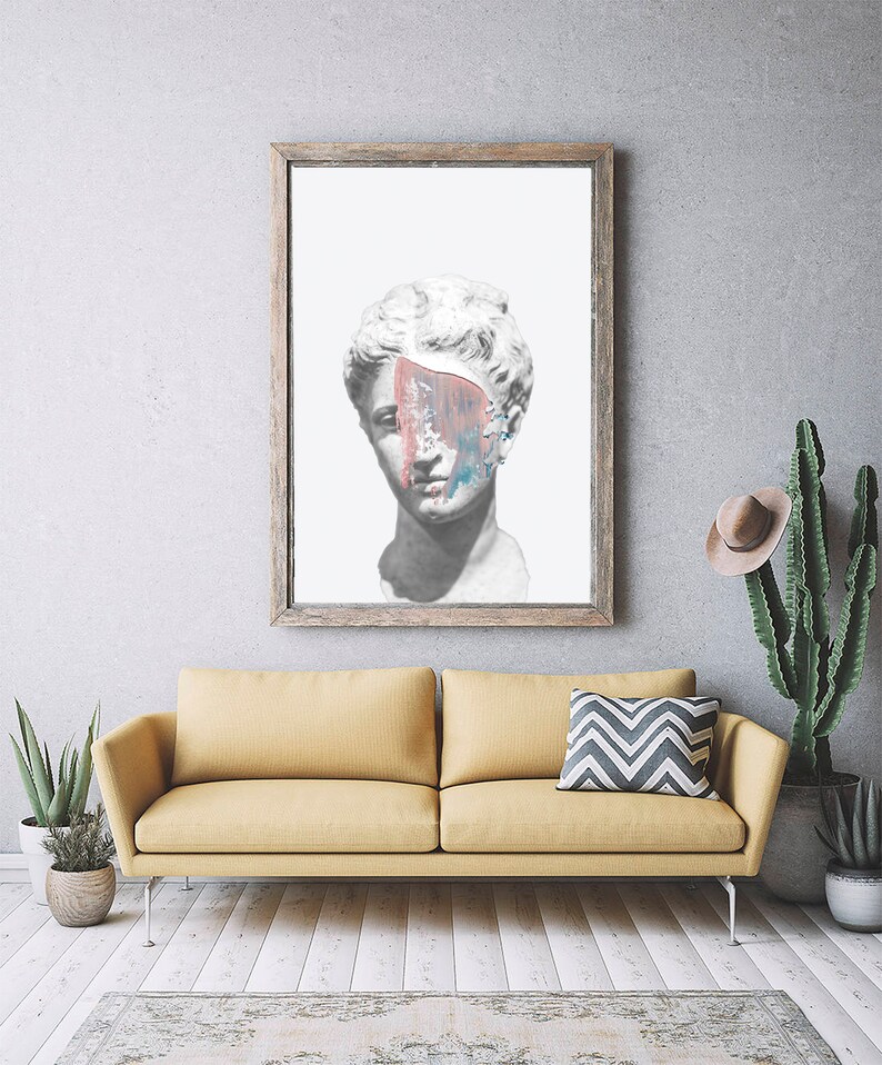 May include: A framed print of a white plaster bust of a woman with a colorful abstract paint splatter covering part of her face. The print is hanging on a gray wall above a yellow sofa.