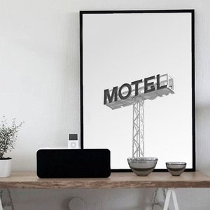 May include: A black and white photograph of a motel sign with the word "MOTEL" in bold letters. The sign is mounted on a tall metal pole. The photograph is framed in a black frame and is hanging on a white wall above a wooden table.