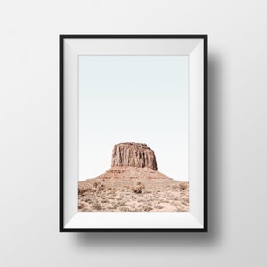 May include: A framed photograph of a large, red rock formation in a desert landscape. The sky is a pale blue and the rock is the focal point of the image.