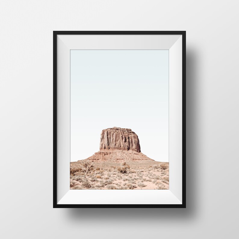 May include: A framed photograph of a large, red rock formation in a desert landscape. The sky is a pale blue and the rock is the focal point of the image.