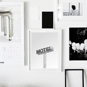 May include: A black and white photograph of a motel sign with the word "MOTEL" in bold lettering. The sign is on a metal pole and is against a white background.