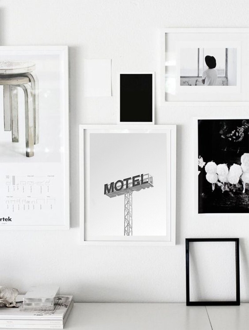 May include: A black and white photograph of a motel sign with the word "MOTEL" in bold lettering. The sign is on a metal pole and is against a white background.