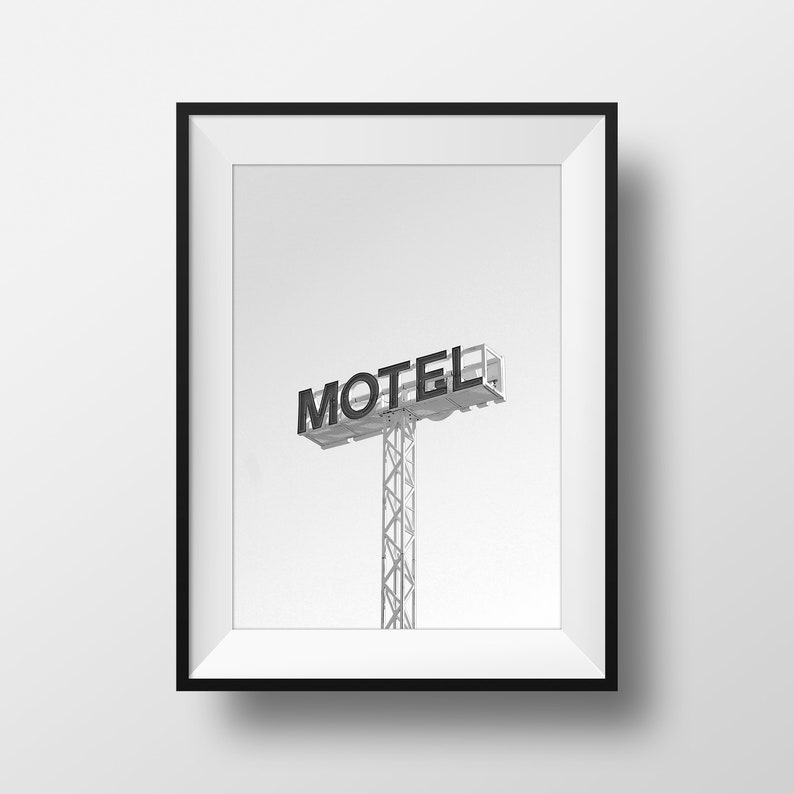 May include: Black and white photograph of a motel sign with the word "MOTEL" in bold letters. The sign is mounted on a tall metal pole.
